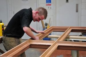 Worker making wooden window frames adding beading