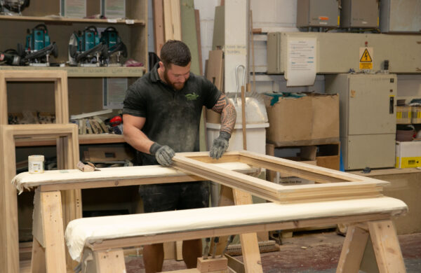 Joiner sands window frame in factory setting.