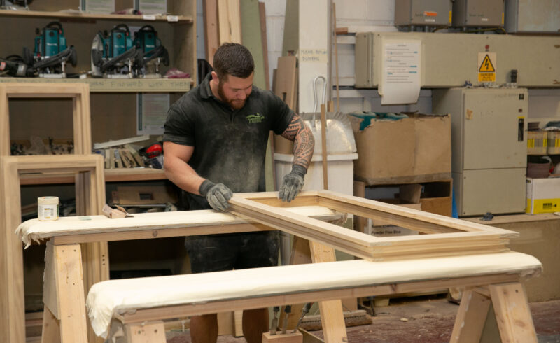 Joiner sands window frame in factory setting.