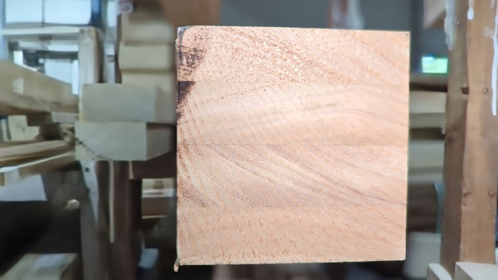 A close-up cross-section of Engineered Red Grandis timber, showing multiple laminated layers of wood with alternating grain directions. This lamination enhances the stability and durability of the timber.