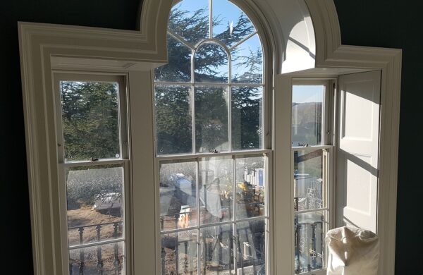 Internal view of three curved-top Palladian-style Winston sliding sash windows with Georgian glazing bars. The windows are framed with custom shutter boxes and painted to match the interior, showcasing a traditional yet functional design that allows for natural light while preserving the building's historic character.