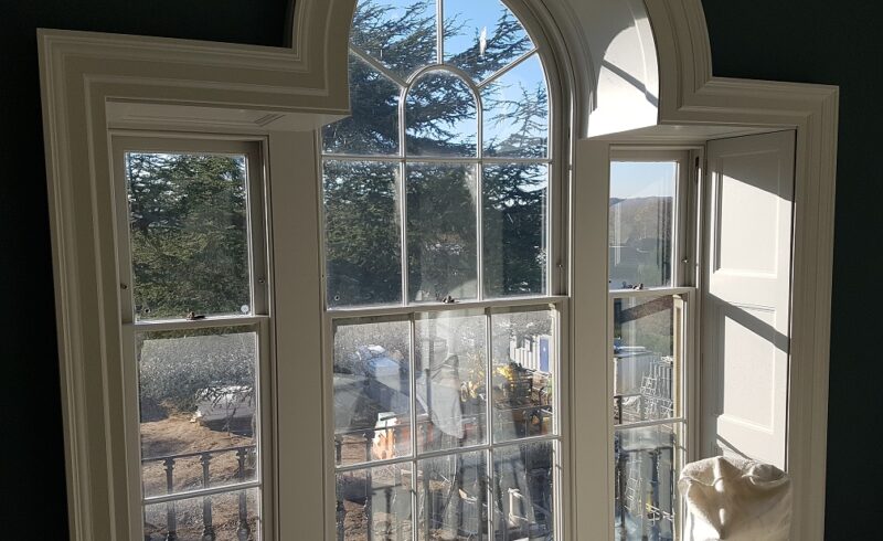 Internal view of three curved-top Palladian-style Winston sliding sash windows with Georgian glazing bars. The windows are framed with custom shutter boxes and painted to match the interior, showcasing a traditional yet functional design that allows for natural light while preserving the building's historic character.