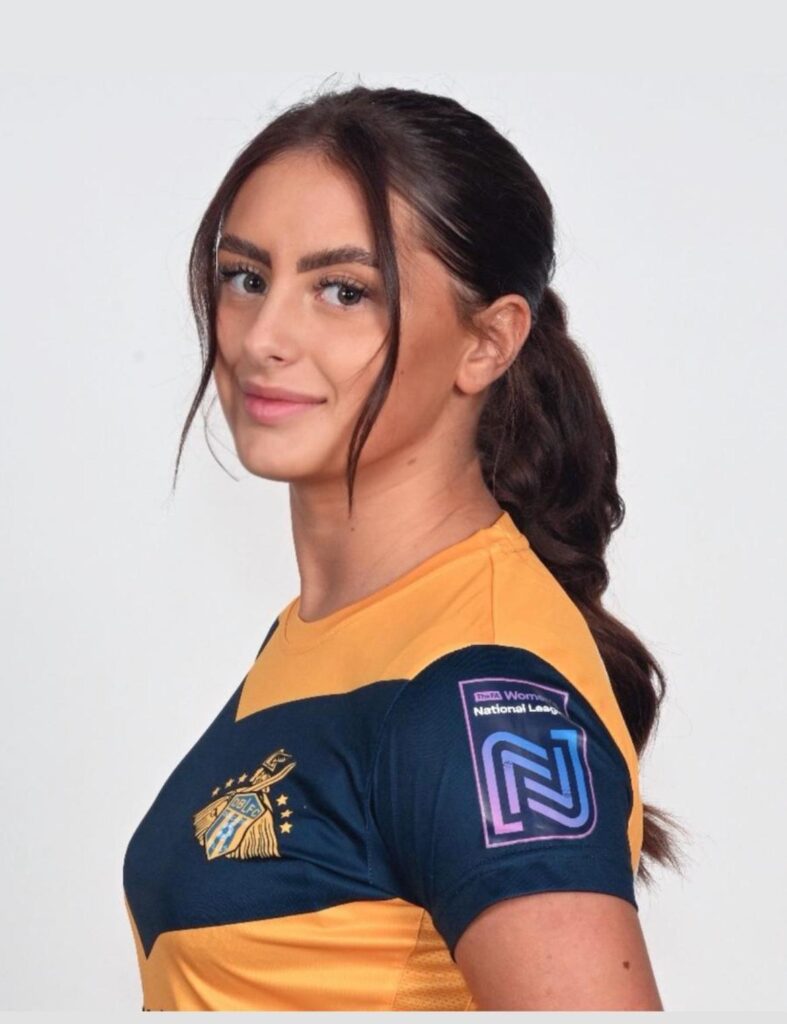 Professional headshot of Lilli-Mae Broadhurst in her Doncaster Belles semi-professional football kit. She is wearing a yellow and navy jersey with the club crest on the chest and the FA Women's National League patch on the sleeve. Her hair is styled in a neat ponytail, and she is smiling confidently with a light backdrop.