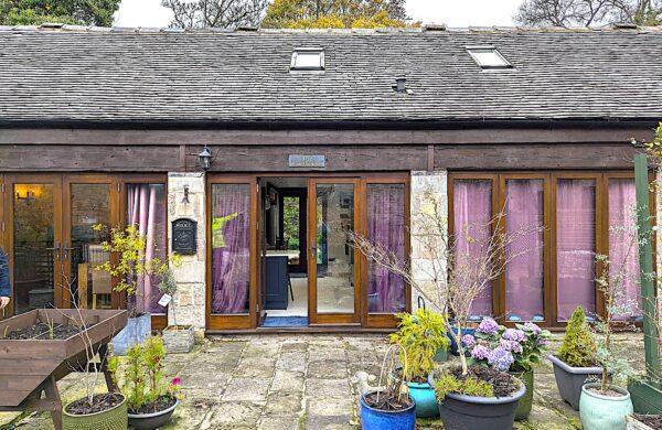 Exterior view of The Carthouse in the Carsington and Hopton conservation area, showcasing Gowercroft Joinery's Melbourne French Doors and Hardwick Casement Windows in Red Grandis timber. Surrounded by stone paving and colourful potted plants, the beautifully restored 19th-century building reflects a seamless blend of heritage aesthetics and modern performance.