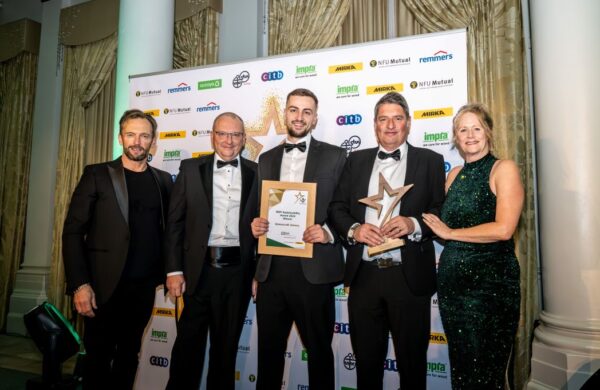 Group photo at the BWF Sustainability Awards 2024 featuring Harry Dixon, Finance Director of Gowercroft Joinery, holding the Sustainability Award certificate, and Darren Young, Production Director, holding the trophy. They are joined by the event host, a judge, and Helen Hewitt, Chief Executive of the British Woodworking Federation, on the right. All are dressed in formal evening wear, standing in front of a branded sponsor wall with elegant curtains and pillars in the background.