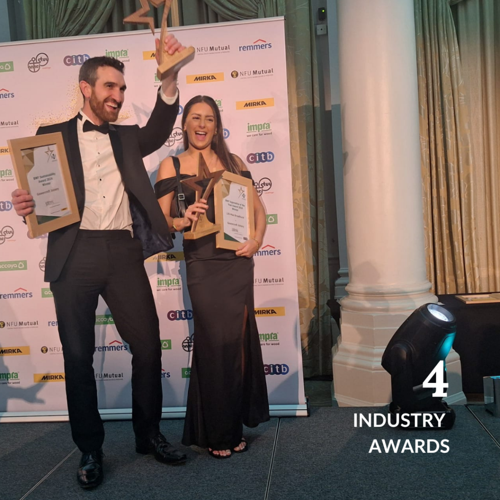 Two Gowercroft Joinery team members celebrating their success on stage, holding trophies and certificates after winning four industry awards in 2024.